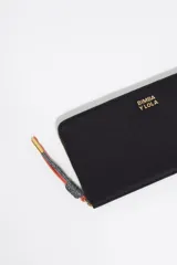 Billetera grande de nylon color negro con cierre perimetral de cremallera. Presenta un tirador de cordón bicolor con terminales metálicos y el logo de la marca estampado en dorado en el frente.
