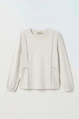 Remera de manga larga color beige con cuello redondo y detalles de encaje calado en la parte frontal. Cuenta con mangas abullonadas y puños elásticos.
