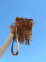 Cartera de gamuza color marrón con diseño de flecos largos en toda la superficie. Cuenta con asas cortas y una correa larga ajustable y extraíble para usar como bandolera.