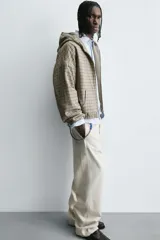 Cazadora boxy fit de algodón con estampado de cuadros en tonos beige y gris. Presenta cuello con capucha, cierre frontal de cremallera, mangas largas con puños elásticos y bolsillos frontales tipo canguro.