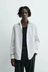 Camisa blanca de corte slim fit, confeccionada en tejido de algodón. Presenta cuello italiano, manga larga con puño abotonado y cierre frontal de botonadura.