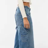 Jean baggy de tiro medio color azul claro con efecto desteñido y roturas en la rodilla izquierda. Presenta bolsillos laterales estilo carpintero y presillas para cinturón.