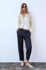 Chaqueta de punto de hilo metalizado color beige con cuello redondo, manga larga y cierre frontal con un botón dorado.