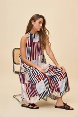 Vestido largo de silueta amplia y caída fluida, con escote halter fruncido y falda con recorte. Presenta diseño geométrico multicolor a rayas en tonos bordó, azul, celeste y beige.