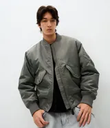 Campera tipo bomber de color verde militar, con cierre frontal, cuello, puños y cintura en tejido rib. Presenta bolsillos frontales con solapa y botón a presión, además de un bolsillo utilitario en la manga.