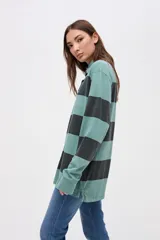 Remera tipo polo de manga larga con diseño de rayas horizontales anchas en bloques de color crema y beige. Presenta cuello camisero con cierre de botones y un pequeño bordado en el pecho.