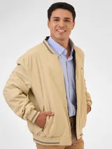 Campera bomber reversible azul marino y beige con cuello, puños y ruedo acanalados con rayas doradas. Tiene cierre frontal y logo bordado en el pecho.