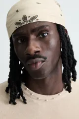 Camiseta de punto color beige claro, corte boxy fit, con cuello redondo y manga corta. Presenta un estampado central en tono similar que simula un efecto spray y acabados irregulares en los bordes.