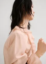 Blusa de lyocell color rosado pálido, de diseño recto con escote en V, detalle de volantes en la solapa y manga larga con puños ajustables.