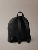 Mochila negra de diseño moderno con acabado tipo piel sintética. Presenta un asa de mano superior, correas ajustables para el hombro, compartimento principal con cremallera y un bolsillo exterior frontal con el monograma 'CK' grabado en relieve.