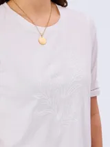 Remera blanca de manga corta 100% algodón, con delicado bordado frontal de diseño botánico y detalles calados en las terminaciones de las mangas.