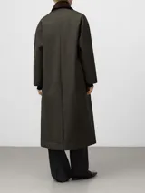 Chaqueta larga de corte recto en color verde oliva, confeccionada en tejido con efecto encerado. Presenta cuello italiano en pana de color contrastante, cierre frontal oculto por solapa y bolsillos de vivo inclinados en el delantero. Diseño de manga larga con acabado suave y ligero.