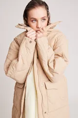 Campera larga acolchada color beige, con diseño de costuras onduladas, cuello alto, cierre frontal con botones a presión y bolsillos laterales amplios.