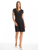 Vestido corto de seda fría color negro, con cuello redondo, mangas cortas tipo casquillo decoradas con perlas y tachas, y corte fluido con caída suave.