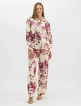 Conjunto de dos piezas compuesto por camisa de manga larga con cuello solapa y botones frontales, y pantalón de tiro alto con pierna recta y bolsillos laterales. Ambas prendas presentan un estampado paisajístico en tonos marrones sobre fondo crema.