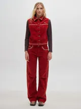 Chaleco de pana color negro con cuello camisero, cierre frontal con botones metálicos dorados, costuras contrastantes en tono claro y pequeño parche distintivo en el pecho.
