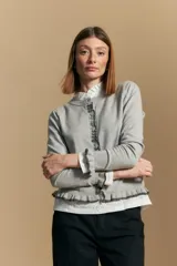 Cárdigan beige de manga larga, tejido liviano y suave, con volados en el delantero, ruedo y puños. Cierre frontal con botones.