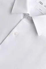 Camisa de corte slim fit confeccionada en tejido de algodón con textura. Presenta cuello italiano, manga larga con puños abotonados y cierre frontal de botones.