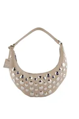 Cartera tipo hobo de Las Oreiro en color beige, con diseño de media luna y decorada con tachas metálicas plateadas en toda su superficie frontal. Incluye una correa fija y un dije colgante con el logo de la marca.