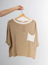 Remera tejida color crema con cuello redondo y bolsillo frontal verde.