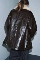 Chaqueta de efecto cuero color marrón oscuro con acabado brillante, cuello de solapa con aplicación de pelo sintético extraíble, manga larga con trabillas, bolsillos frontales de plastrón con solapa y cierre frontal con cremallera y botones a presión.