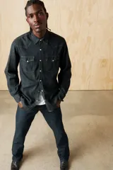 Camisa de denim azul oscuro con corte clásico, mangas largas, cierre con botones a presión, dos bolsillos frontales con solapa y costuras decorativas en los hombros.