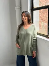 Sweater de punto color verde, con escote en V, mangas largas con puños acanalados y dos bolsillos frontales. Presenta una costura vertical central decorativa.