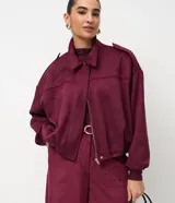 Campera bomber color bordó de gamuza sintética, con cuello clásico, cierre frontal y hombros caídos con tirilla decorativa en los hombros.