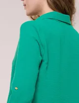 Blusa verde de calce holgado y caída fluida, confeccionada en tejido tipo crepé. Cuenta con cuello camisero con solapa, escote en V y cierre parcial al frente con tres botones metálicos. Las mangas son largas con puños abotonados.