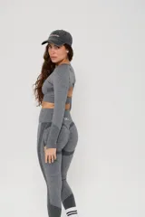 Conjunto deportivo de dos piezas compuesto por un top de manga larga con abertura en la espalda y calzas de tiro alto con diseño de contorno moldeador. Ambas prendas presentan un acabado jaspeado y detalles de tejido técnico con textura.