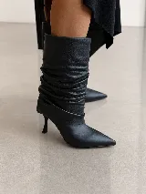 Bota de caña media en cuero negro, con diseño de efecto arrugado en la caña, punta fina y taco fino de altura media.