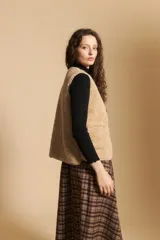 Chaleco de textura tipo corderito en color beige, con cierre frontal de botones a presión y bordes ribeteados. Presenta un diseño sin mangas con silueta relajada.
