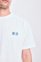 Camiseta blanca de manga corta con corte oversize y estampa en la espalda de una ola, un sol y tres aves. Incluye texto en japonés.