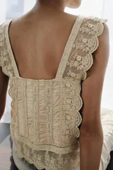 Top de estilo corset confeccionado en viscosa satinada color beige. Presenta escote recto, tirantes anchos con terminación de encaje, detalle de pliegues verticales, lazada frontal y aplicaciones de encaje con bordados florales en el cuerpo y el ruedo.
