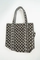 Bolso tipo tote acolchado con estampado floral en tonos oscuros y detalles de ribetes a rayas en blanco y negro.