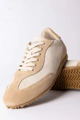 Championes urbanos de diseño retro, confeccionados en una combinación de gamuza y cuero texturizado en tonos beige y arena. Presentan cordones al tono y una suela dentada de goma en color caramelo.