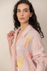 Camisa de lino rosada con mangas largas, cuello camisero y bordados coloridos de motivos veraniegos repartidos en el frente.