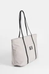 Cartera tipo shopper color beige con asas y detalles decorativos en cuero sintético negro. Cuenta con un bolsillo frontal exterior adornado con una etiqueta rectangular de la marca Symphorine.