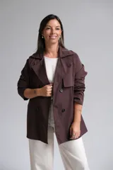 Trench corto color chocolate, con cuello solapa, cierre frontal cruzado con botones y mangas largas.