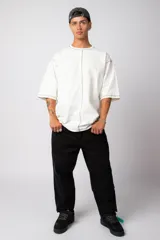 Remera de corte oversize color malva, confeccionada en algodón pesado, con costuras externas visibles en color blanco que recorren el centro, el cuello y los bordes de las mangas.