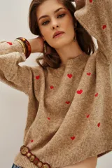 Sweater de punto color beige melange con bordado de pequeños corazones rojos distribuidos por toda la prenda. Posee cuello redondo, mangas largas y terminaciones acanaladas en puños y ruedo.