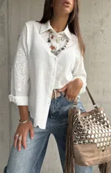 Camisa blanca de corte clásico con cuello camisero y cierre frontal de botones. Presenta un delicado bordado tono sobre tono en las mangas y una textura sutil en la tela.
