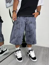 Pantalón ancho estilo baggy, color azul grisáceo, con estampado abstracto en negro. Presenta un diseño desmontable que permite convertirlo en un pantalón corto o bermuda, con cierres a la altura de la rodilla.
