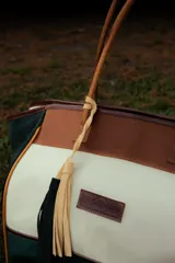 Bolso de fin de semana estilo tote de lona con estampado camuflado, detalles en cuero marrón y gamuza azul, manijas largas y borla decorativa colgante.
