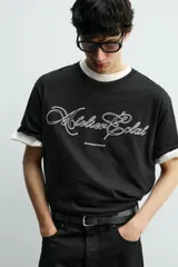 Camiseta de corte relajado color negro, con cuello redondo y manga corta. Presenta un bordado frontal con texto en color blanco a contraste.