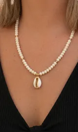 Collar de cristales facetados beige con dije central de caracola natural con detalles dorados y esferas metálicas doradas intercaladas.