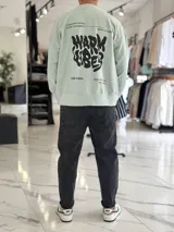 Buzo oversize color beige, con diseño gráfico en la espalda con el texto 'Warm Vibes' en tono marrón y tipografía psicodélica, acompañado de frases secundarias.