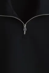 Buzo negro de tejido pesado con efecto neopreno, cuello elevado y medio cierre frontal plateado. Presenta hombros caídos, mangas largas y puños y bajo acanalados.