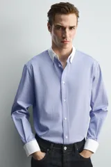 Camisa de corte regular fit confeccionada en tejido ligero de algodón, con diseño de rayas verticales azules y blancas. Presenta cuello abotonado y puños en color blanco a contraste, con cierre frontal de botones.