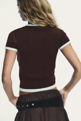 Chaqueta de punto marrón de manga corta, con cuello redondo y ribetes en color celeste claro. Presenta cierre frontal con botones nacarados.